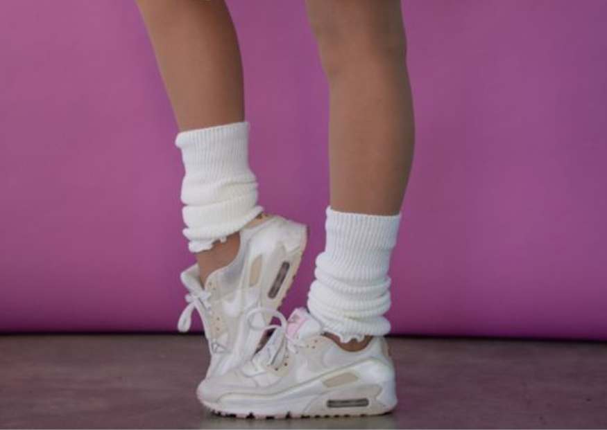 Persona in posa su sfondo rosa con outfit in stile anni ’80: body, cintura, scaldamuscoli e scarpe da ginnastica. Tiene in mano un lettore stereo portatile.